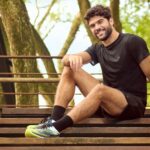 Homem com roupa fitness preta e tênis de academia sentado em uma escada ao ar livre.