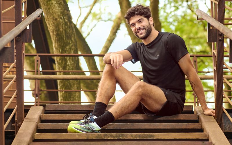 Homem com roupa fitness preta e tênis de academia sentado em uma escada ao ar livre.