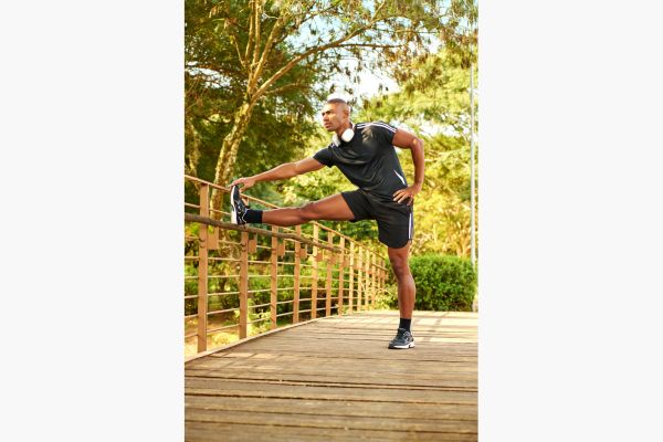 homem usa roupa fitness e tênis esportivo enquanto se alonga. 