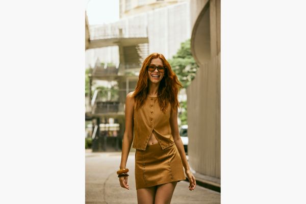 mulher veste conjunto de suede. Saia e colete com detalhe de tachas.