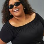 modelo veste blusa preta ombro a ombro plus size e óculos de sol