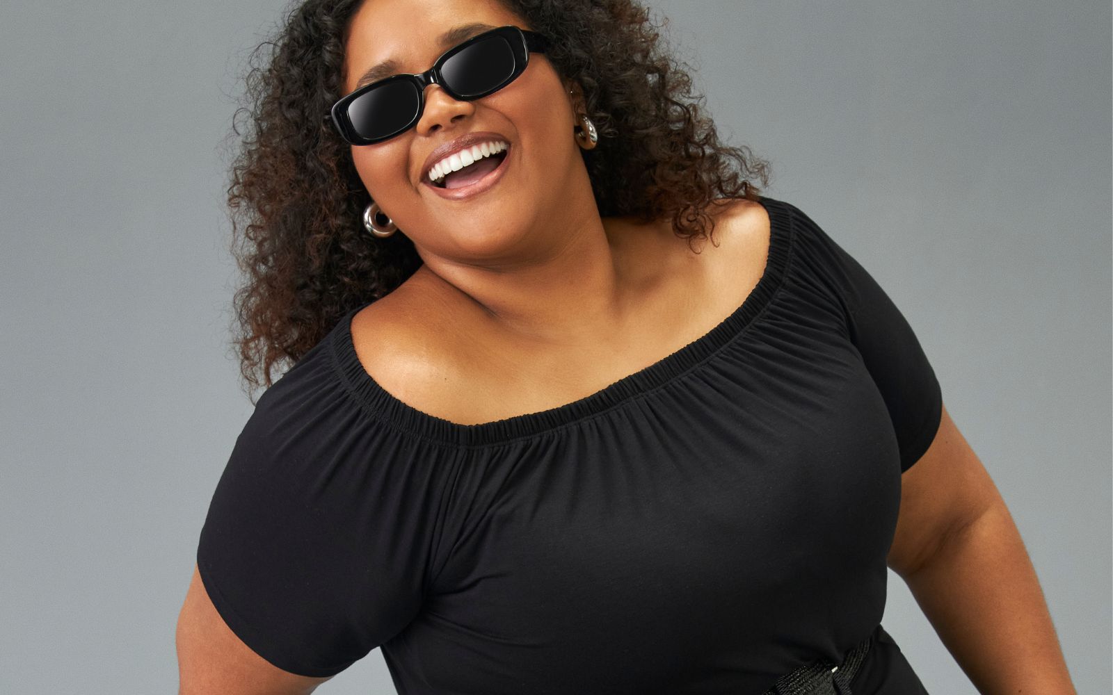 modelo veste blusa preta ombro a ombro plus size e óculos de sol