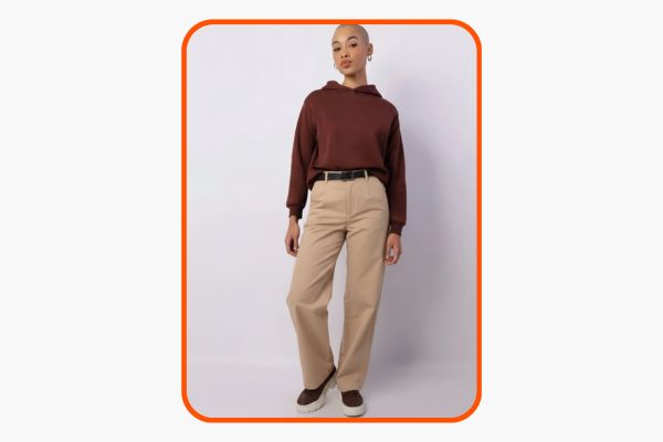 Mulher veste moletom marrom com calça de alfaiataria bege.