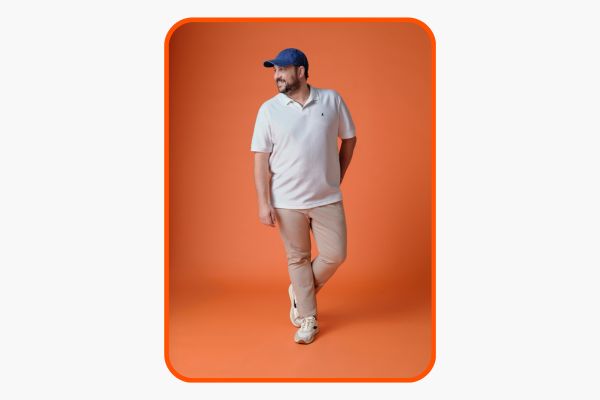 Homem veste camisa polo masculina plus size branca com calça bege e boné azul.