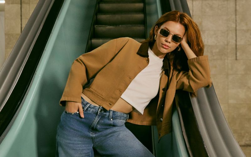 modelo veste calça jeans, blusa cropped branca básica abaixo de casaco.