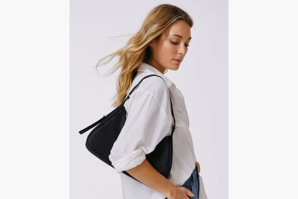 Modelo veste camisa branca básica, mas o foco da foto é a sua bolsa preta da moda.