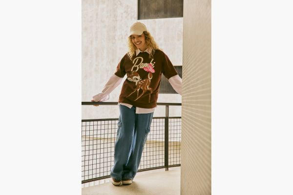 mulher veste calça jeans cargo feminina com camiseta do Bambi sobre uma camisa. Finaliza o look com boné.