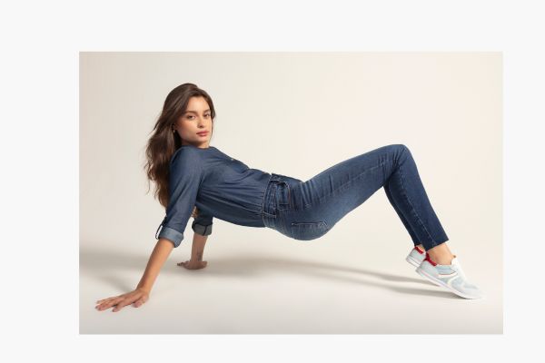 modelo veste um look todo em jeans, camisa e calça, e um tênis azul claro com detalhe em vermelho.