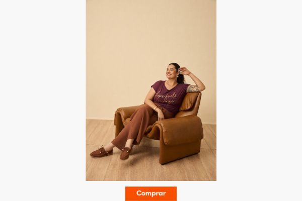 Modelo sentada em cadeira estilosa, usando camiseta roxa