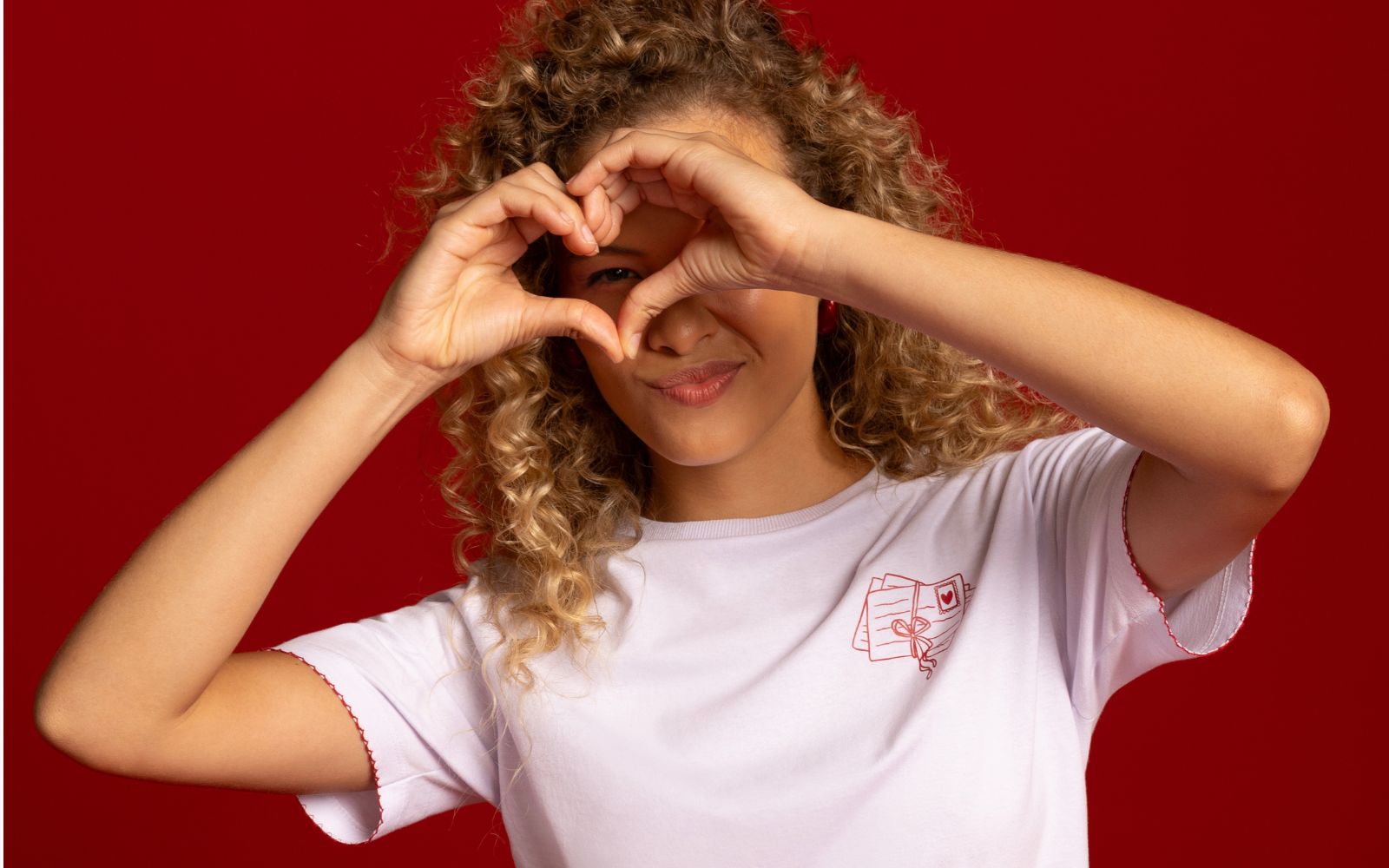 Modelo veste camiseta branca e faz coração com as mãos, o fundo da imagem é vermelho como a cor da campanha de Liquidação da Torra