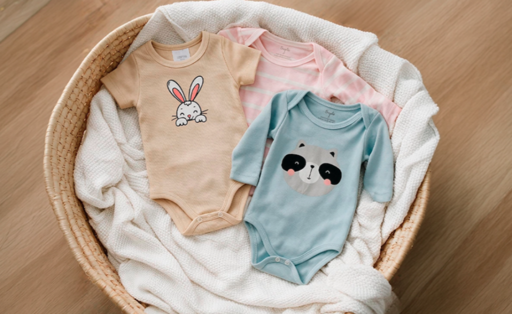 Bodies de bebê Torra com estampas de coelho, listras e guaxinim, dobrados em cesta de vime