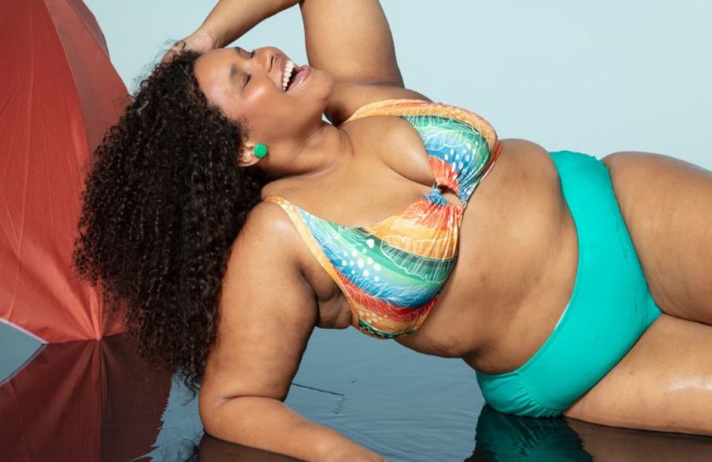 Mulher debruçada passa a mão no cabelo enquanto veste um look plus size para praia