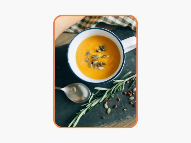 tigela com sopa laranja e um ramo de alecrim do lado