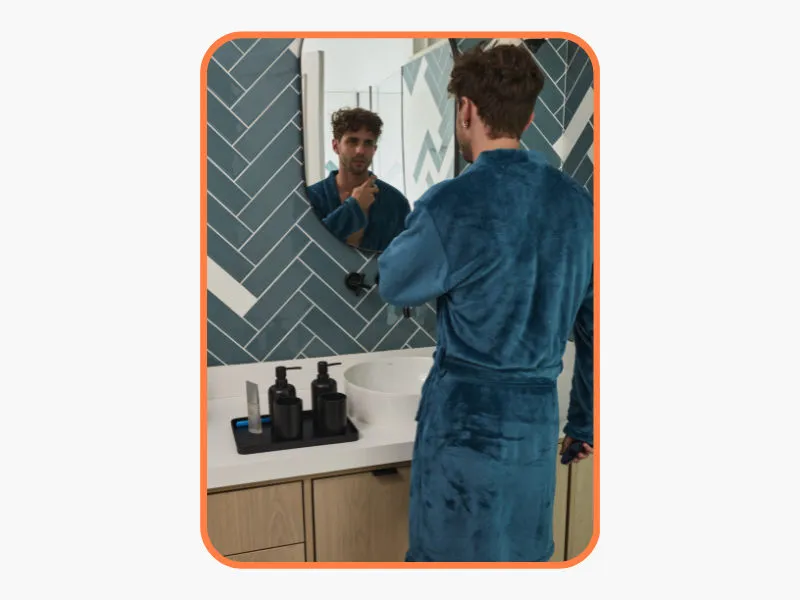 homem com um roupão azul se olhando no espelho do banheiro com expressão séria