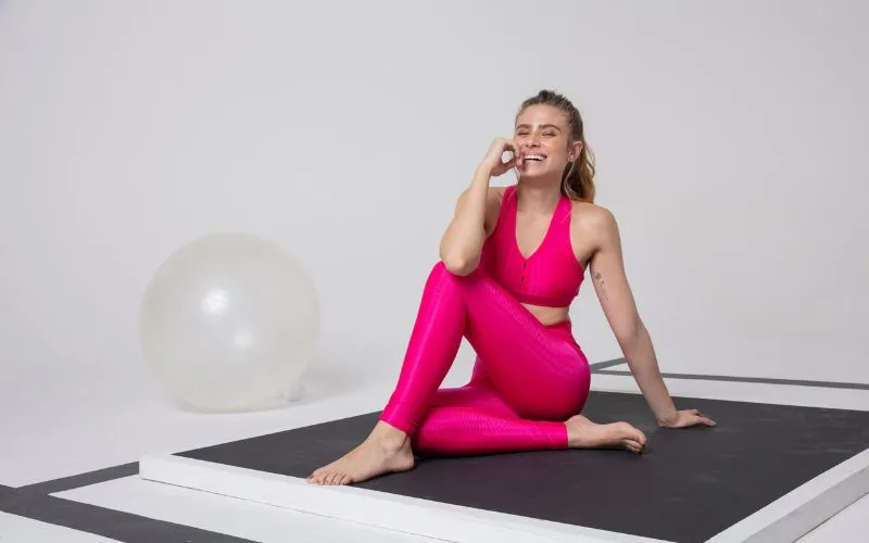 mulher praticando ioga enquanto usa um conjuntinho de legging e top rosa